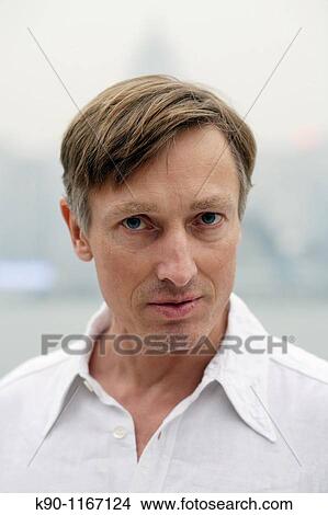 Picture - Portrait of caucasian man, looking at the camera, with the silhouette of the buildings of Hong Kong Island in the background, Hong Kong, China, Far East Asia. Fotosearch