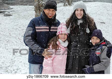 Stock Photo - Portrait of happy Caucasian family of four posing in snow smiling. Fotosearch