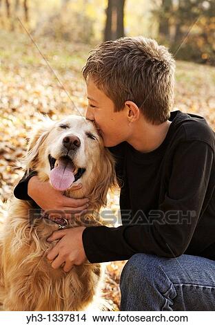 Picture - Portrait of happy young boy kissing his golden retriever dog at the park. Fotosearch