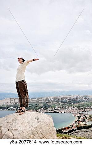 Portrait of smiling mid adult woman with outstretched arms standing on rock. View Large Photo Image Picture - Portrait of smiling mid adult woman with outstretched arms standing on rock.. Fotosearch