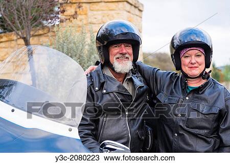 Stock Image - Portrait of two mature motorcyclists wearing black leather outfit and helmets while looking at camera.. Fotosearch