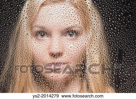 Stock Photo - Portrait of young blond female teenager looking out of window covered with raindrops.. Fotosearch
