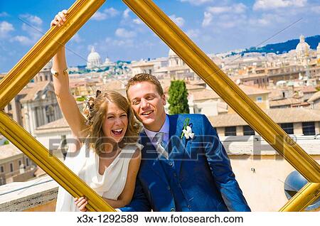 Stock Photo - Portrait of young bride and groom holding picture frame in Rome, Italy. Fotosearch