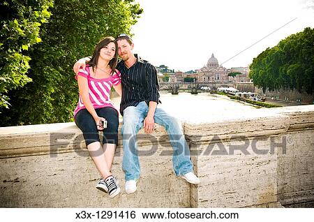 Portrait of young couple sitting on ledge with Saint Peter Basilica behind, Rome, Italy View Large Photo Image Stock Photograph - Portrait of young couple sitting on ledge with Saint Peter Basilica behind, Rome, Italy. Fotosearch