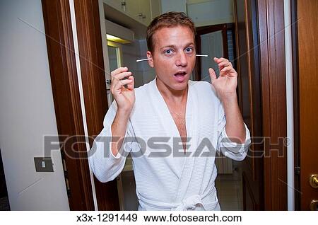 Stock Photo - Portrait of young man in bathrobe with q-tips in ears. Fotosearch