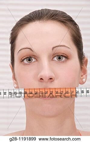 Portrait of young woman, hiding her mouth with a measuring tape in her bathroom View Large Photo Image Stock Photo - Portrait of young woman, hiding her mouth with a measuring tape in her bathroom. Fotosearch