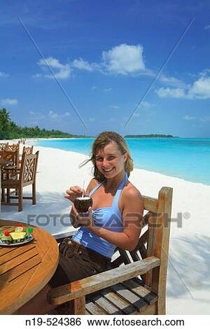 Stock Photograph - Portrait of young woman on the beach with cocktail, Maldives, Indian ocean. Fotosearch