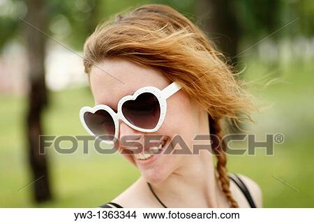 Portrait of young woman outdoors with heart-shaped sunglasses View Large Photo Image Picture - Portrait of young woman outdoors with heart-shaped sunglasses. Fotosearch