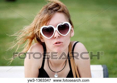Portrait of young woman outdoors with heart-shaped sunglasses View Large Photo Image Stock Photo - Portrait of young woman outdoors with heart-shaped sunglasses. Fotosearch