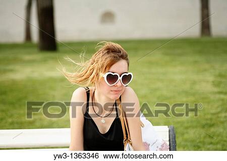 Stock Photograph - Portrait of young woman outdoors with heart-shaped sunglasses. Fotosearch