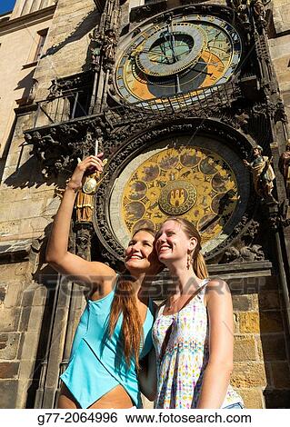 Stock Photograph - Prague. Czech Republic. Two young women taking picture in front of the Astronomical Clock with a smart phone.. Fotosearch