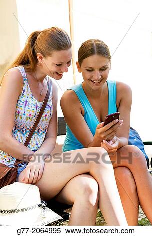 Prague. Czech Republic. Two young women sitting on a bench watching a smart phone. View Large Photo Image Stock Photography - Prague. Czech Republic. Two young women sitting on a bench watching a smart phone.. Fotosearch