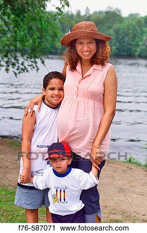 Stock Image - Pregnant Brazillian woman wearing straw hat, alongside river with her two young boys.. Fotosearch