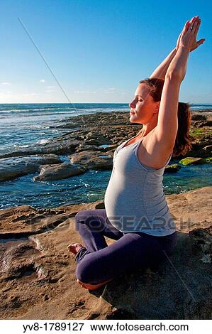 Stock Photo - Pregnant woman doing yoga on rocks. Fotosearch