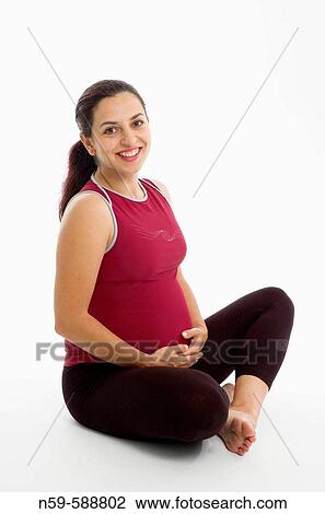 Pregnant woman in exercise clothes sits corss legged holding her bump. View Large Photo Image Stock Image - Pregnant woman in exercise clothes sits corss legged holding her bump.. Fotosearch