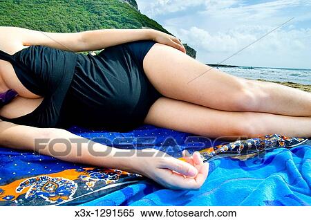 Stock Photography - Pregnant woman laying down on the beach by the sea. Fotosearch