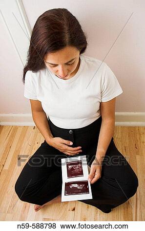 Stock Photo - Pregnant woman looking at her unborn child on print of her ultrasound scan.. Fotosearch