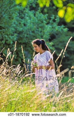 Stock Image - Pregnant woman picking meadow flowers. Fotosearch