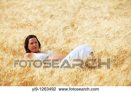 Stock Image - Pregnant woman relaxing in field. Fotosearch