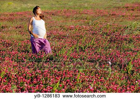 Stock Image - Pregnant woman relaxing in field. Fotosearch