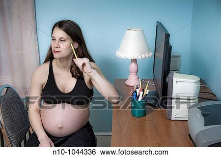 Pregnant woman sitting at her desk, holding a pencil View Large Photo Image Stock Photograph - Pregnant woman sitting at her desk, holding a pencil. Fotosearch