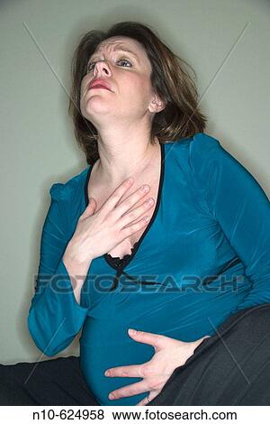 Stock Photo - Pregnant woman sitting on her bed, her hand on her belly.. Fotosearch