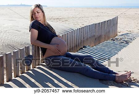 Stock Photo - Pregnant woman sitting on the beach with eyes closed.. Fotosearch