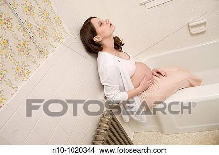 Pregnant woman sitting on the edge of her bathtub View Large Photo Image Picture - Pregnant woman sitting on the edge of her bathtub. Fotosearch