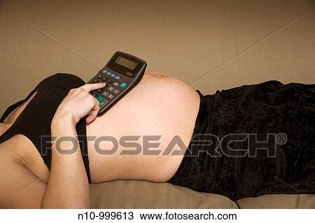 Stock Image - Pregnant woman using a calculator that sits on her belly. Fotosearch