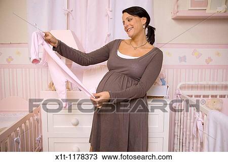 Stock Image - Pregnant woman with baby clothes.. Fotosearch