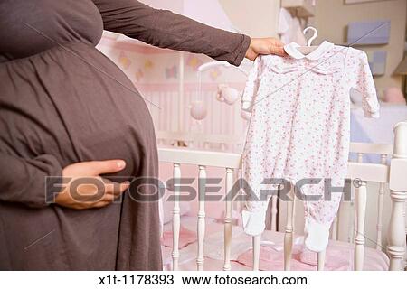 Stock Image - Pregnant woman with baby clothes.. Fotosearch