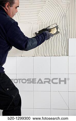 Stock Image - Preparing wall with glue mortar before tiling using a serrated plastering trowel, new homes under construction, construction site. Fotosearch