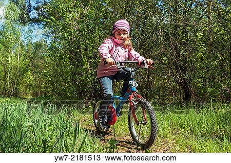 Stock Image - Preschool girl riding her bicycle in a forest.. Fotosearch