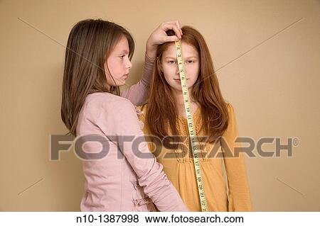 Stock Photo - Preteen girl measuring her friend with a tape measure. Fotosearch