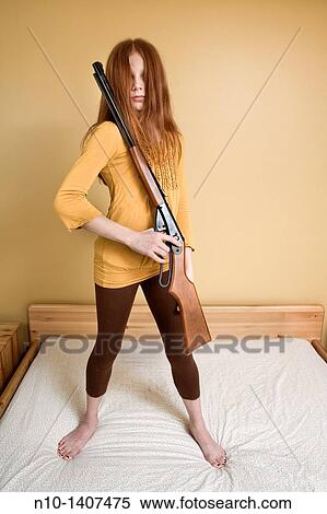 Stock Photography - Preteen girl, standing on her bed, holding a rifle. Fotosearch