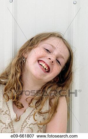 Stock Photo - Preteen girl with wavy golden-brown hair and freckles, laughing with head toward one shoulder, leaning against white shed. Fotosearch