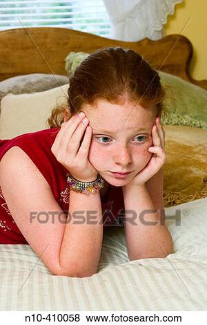 Stock Photo - Preteen redhead girl, in Connecticut, USA, reclining on her mother's bed, thinking.. Fotosearch