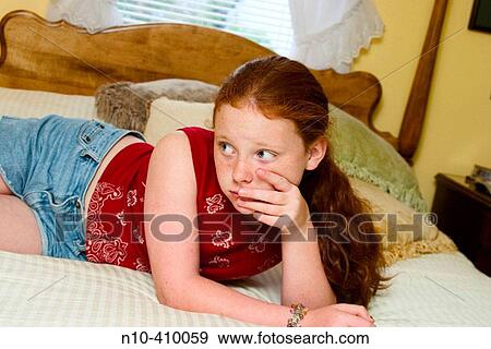 Stock Photo - Preteen redhead girl, in Connecticut, USA, reclining on her mother's bed, thinking.. Fotosearch
