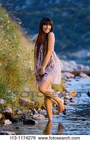Stock Photo - Pretty and shy young woman is walking on the coastline. Fotosearch