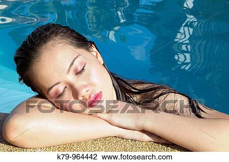 Stock Image - Pretty Asian young woman relaxing in swimming pool with eyes closed.. Fotosearch
