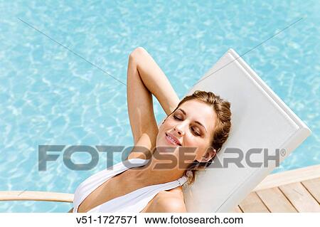Stock Image - Pretty blonde woman enjoying the sun in a hammock by the pool. Fotosearch