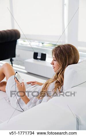 Picture - Pretty blonde woman listening to music on the sofa. Fotosearch