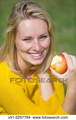 Pretty blonde woman with apple in park View Large Photo Image Picture - Pretty blonde woman with apple in park. Fotosearch