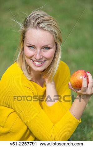 Stock Image - Pretty blonde woman with apple in park. Fotosearch