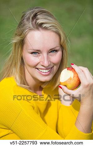 Stock Image - Pretty blonde woman with apple in park. Fotosearch