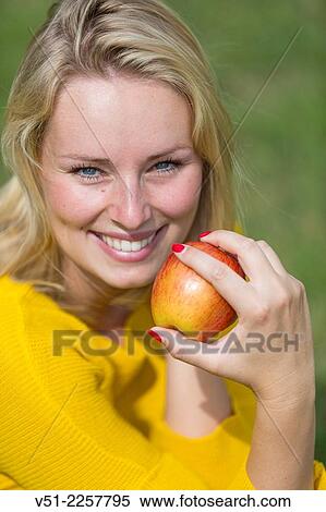 Stock Photography - Pretty blonde woman with apple in park. Fotosearch