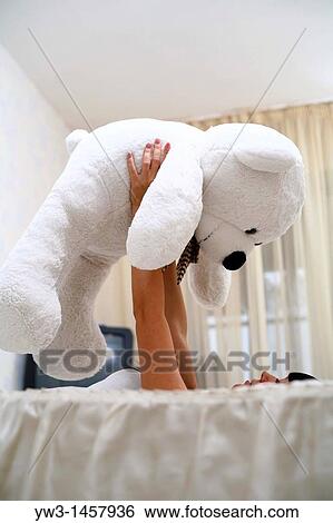 Stock Photograph - pretty brunette girl indoors embracing with big teddy bear on sofa. Fotosearch