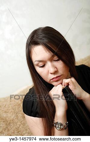 Picture - pretty brunette girl indoors on modern sofa. Fotosearch