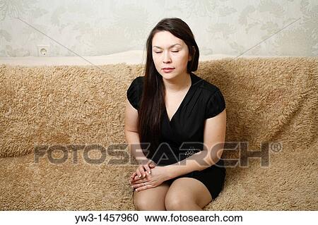Stock Image - pretty brunette girl indoors on modern sofa. Fotosearch