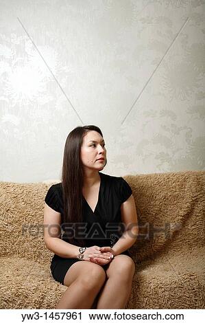 Stock Image - pretty brunette girl indoors on modern sofa. Fotosearch